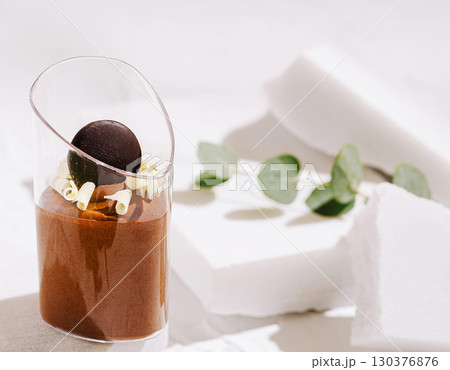 Chocolate dessert served in a glass with garnishes on a white table 130376876