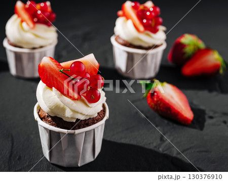 Delicious chocolate cupcakes topped with fresh strawberries and berries 130376910