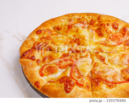 Freshly baked cheese pizza with tomato slices on a marble countertop Freshly baked cheese pizza with tomato slices on a marble countertop 130376990