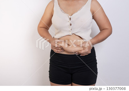 Overweight woman hand pinching excessive belly fat on gray background, Healthy concept Overweight woman hand pinching excessive belly fat on gray background, Healthy concept 130377008