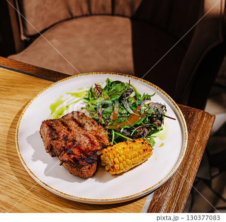 Delicious grilled steak with corn and fresh salad served at a modern restaurant Delicious grilled steak with corn and fresh salad served at a modern restaurant 130377083