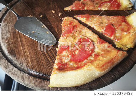 An uneaten slice of pizza with tomatoes and cheese on a wooden stand on a table in a restaurant 130379458