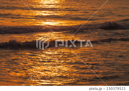 Golden hues of sunset reflecting on rippling ocean waves 130379521