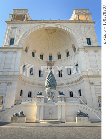 Fontana della Pigna or the Pinecone Fountain, in Vatican known for its massive bronze pine cone sculpture flanked by two peacocks and marble basin, with view to the large arched Neoclassical building 130379807