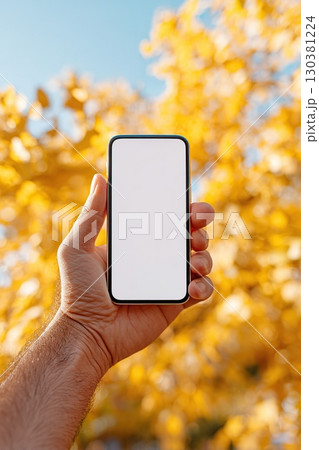 Person holding a vertical phone against a backdrop of vibrant yellow foliage outdoors 130381224