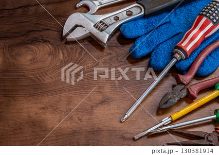 Different working tools on dark wooden background. Hand tools and the Flag of the United States of America lying on the table. View from above, close-up. National USA holiday celebration concept Different working tools on dark wooden background. Hand tools and the Flag of the United States of America lying on the table. View from above, close-up. National USA holiday celebration concept 130381914