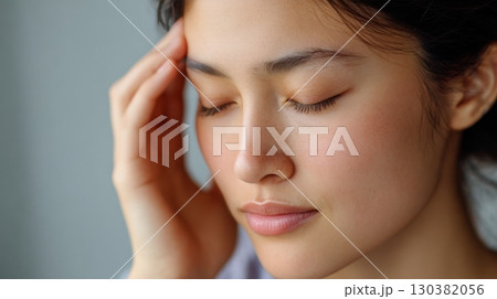 A young woman appears to be in discomfort, resting with eyes closed and a hand on her forehead 130382056