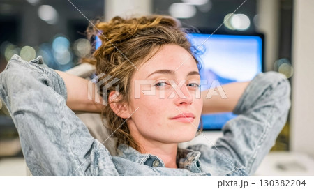Young woman with tousled hair relaxing in a modern office environment, exuding confidence and calmness while seated at her desk 130382204