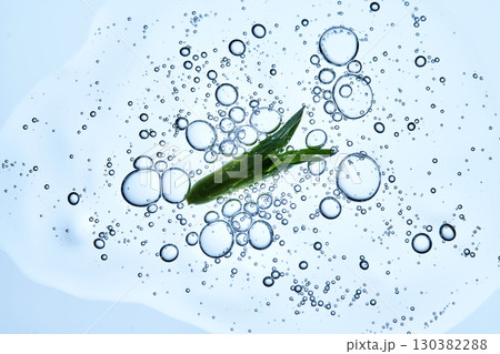 A drop of serum with bubbles and a green leaf on a blue background. A drop of serum with bubbles and a green leaf on a blue background. 130382288