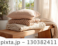 Cozy cotton throws neatly stacked on a natural wooden bench in a sunlit room 130382411