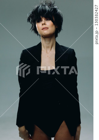 Stylish woman with short black hair wearing a black blazer against a neutral background, exuding modern confidence and minimalistic elegance. 130382427
