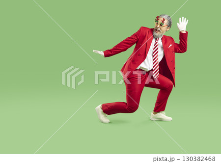 Young Santa Claus dressed in stylish red suit and striped tie is fooling around and dancing. 130382468