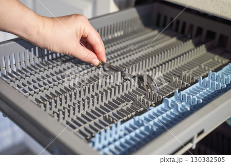 Female hand adjusting cutlery in dishwasher rack for efficient kitchen appliance Female hand adjusting cutlery in dishwasher rack for efficient kitchen appliance 130382505