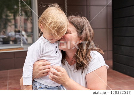 Caucasian female adult hugging blonde caucasian young child smiling on porch Caucasian female adult hugging blonde caucasian young child smiling on porch 130382517