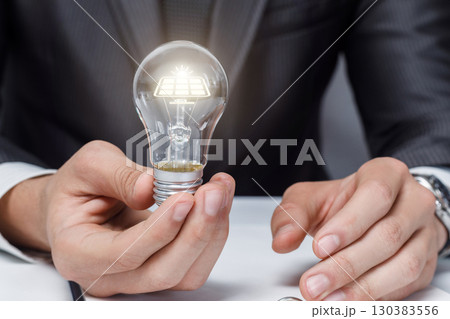 Innovative man holds a light bulb with solar technology. 130383556