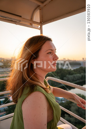 Woman in a green dress enjoys a sunset view from a high vantage point, with sunlight illuminating her hair 130383910
