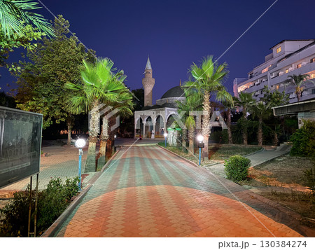 Illuminated mosque with dome and minaret stands among palm trees at night. Religion, architecture and culture reflecting faith, heritage and community in urban environment. Illuminated mosque with dome and minaret stands among palm trees at night. Religion, architecture and culture reflecting faith, heritage and community in urban environment. 130384274