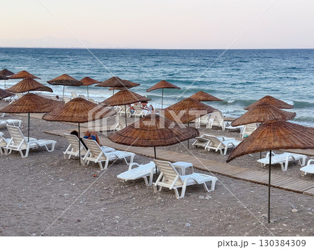 Beach with straw umbrellas and sun loungers by the sea. Summer vacation, relaxation and coastal leisure lifestyle. 130384309