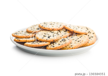 Crispy round salted crackers with sesame seeds on plate isolated on white background. Crispy round salted crackers with sesame seeds on plate isolated on white background. 130384351