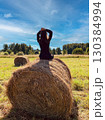 A woman is sitting on a hay bale in a field. 130384994