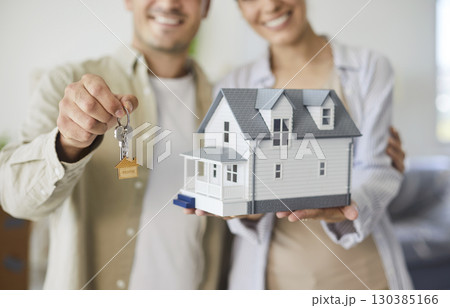 Smiling couple holding house keys and model, celebrating first home purchase 130385166
