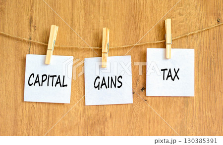 Capital gains tax symbol. Concept words Capital gains tax on beautiful white paper on wooden clothespin. Beautiful wooden background. Business and capital gains tax concept. Copy space. 130385391