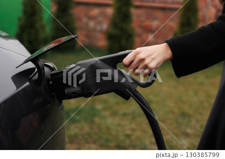 Unrecognisable woman inserting EV charger plug from public or home charging station for modern electric or hybrid car at special place for e-car. Concept eco-friendly sustainability energy car Unrecognisable woman inserting EV charger plug from public or home charging station for modern electric or hybrid car at special place for e-car. Concept eco-friendly sustainability energy car 130385799