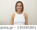 Portrait of young smiling caucasian european attractive woman 30s with straight-shoulder length brown hair in white tank top looking at camera isolated on light background. People lifestyle concept. 130385801