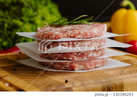 Stack of raw burger patties with rosemary on parchment paper, prepared for grilling Stack of raw burger patties with rosemary on parchment paper, prepared for grilling 130386265