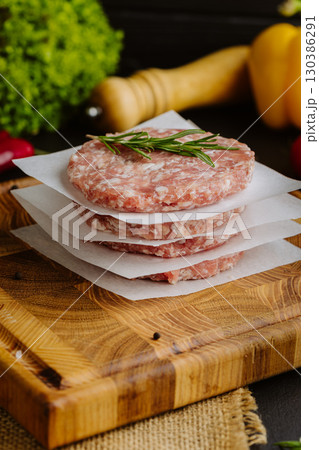 Stack of raw burger patties with rosemary on parchment paper, prepared for grilling 130386291