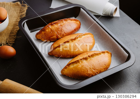 Golden homemade pies in baking tray, rustic kitchen scene with rolling pin and eggs 130386294
