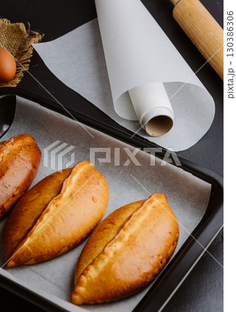 Golden homemade pies in baking tray, rustic kitchen scene with rolling pin and eggs Golden homemade pies in baking tray, rustic kitchen scene with rolling pin and eggs 130386306