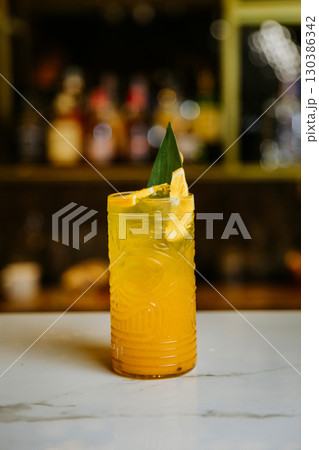 Refreshing tropical cocktail in a tiki glass with citrus garnish on a bar counter 130386342
