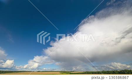A stunning, majestic cloudscape and rainbow beautifully graces the serene and peaceful landscape below 130386867