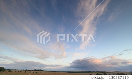 The Stunning Sunset Sky is adorned with Wispy Clouds gracefully drifting Over Rolling Fields 130387110