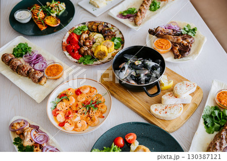 Top view of assorted grilled meats, seafood, and side dishes on a restaurant table 130387121