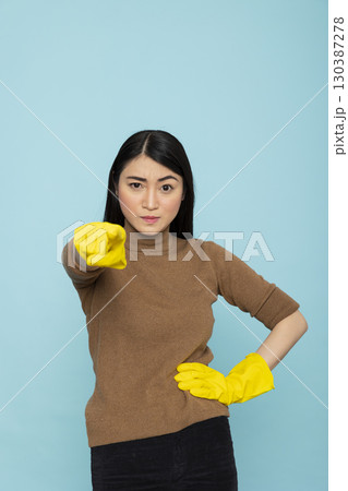 Portrait of beautiful asian woman standing in rubber gloves, pointing directly at camera with serious expression. Confident housemaid expresses confrontation and stress of housekeeping. 130387278