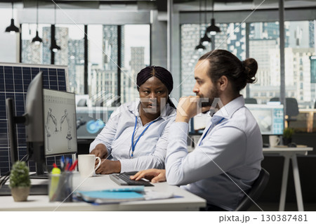 Team of engineers brainstorming solar panel cells with reduced carbon footprint designs. Teamworking colleagues in office develop robotic arm systems for automated clean energy solar panel production Team of engineers brainstorming solar panel cells with reduced carbon footprint designs. Teamworking colleagues in office develop robotic arm systems for automated clean energy solar panel production 130387481