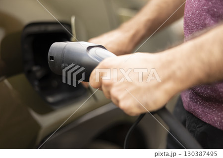 Close up of person unplugging electric car from power supply after battery is full, concept of sustainability commitment. Driver disconnecting EV vehicle from charging dock 130387495