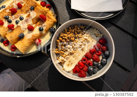 European breakfast with pancakes and healthy fruit bowl on dark wooden table 130387502