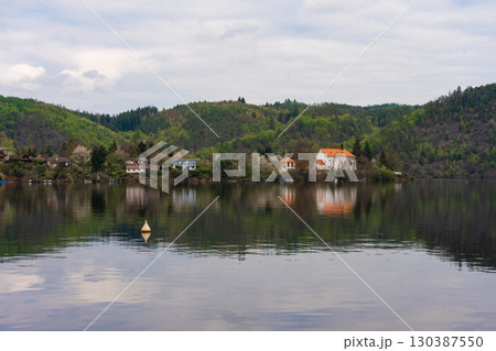 Riverside village with forested hills and cottages reflected in calm water near Nova Zivohost Riverside village with forested hills and cottages reflected in calm water near Nova Zivohost 130387550
