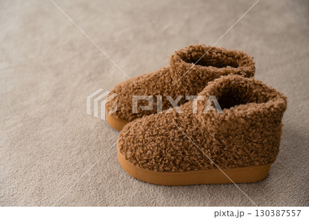 Warm brown fleece boots with textured sole and curly wool upper on soft beige carpet, copy space 130387557