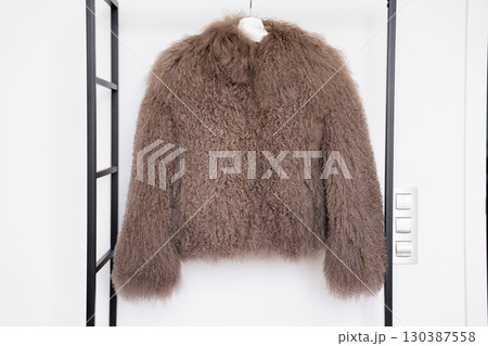 Grey Mongolian lamb wool coat with long curly texture on hanger in bright retail display. 130387558