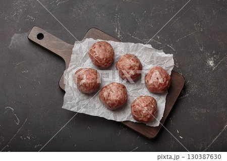 Raw meatballs sitting on wooden cutting board with parchment paper 130387630