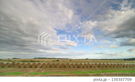 A beautiful and scenic rural landscape featuring hay bales beneath a cloudy sky above 130387709