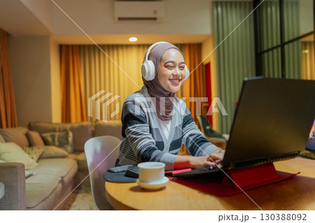 Young woman working remotely on her laptop in a cozy living room, enjoying tech 130388092