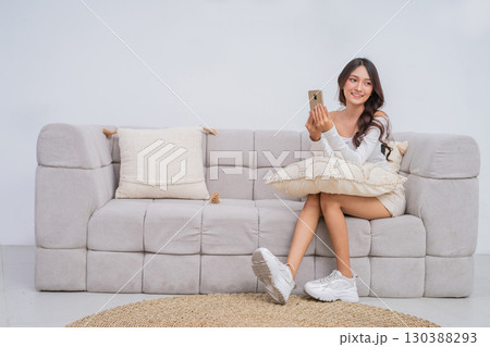 A Young Woman Resting Comfortably on a Couch while Holding Her Phone with a Bright Smile 130388293