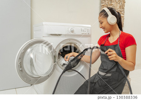 Young woman enjoying laundry time with headphones in a modern washroom Young woman enjoying laundry time with headphones in a modern washroom 130388336