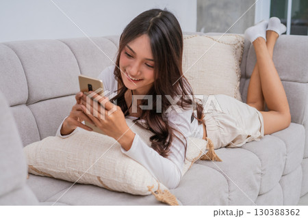 A young woman is relaxing comfortably on her couch at home while using her smartphone 130388362