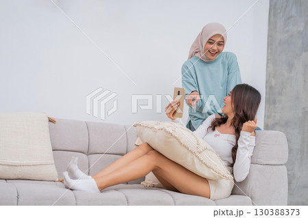 Two Friends Having a Wonderful and Fun Time While Relaxing on the Couch with a Smartphone 130388373